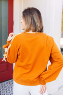 Woman wearing a toffee sweatshirt with white ribbon detail standing in front of Laundry Dae Boutique.