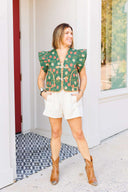 Woman wearing a green floral vest and white shorts standing outside boutique.