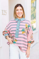Woman wearing a colorful striped sweatshirt with floral patterns in an outdoor setting.