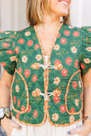 Woman wearing a green floral vest and white shorts standing outside boutique.