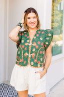 Woman wearing a green floral embroidered vest over a white outfit, standing outdoors.