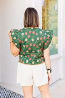 Woman wearing a green floral vest and white shorts standing outside boutique.