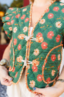 Green floral-patterned vest with orange accents held by a person.