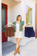 Woman wearing ivory corduroy shorts, holding two other color options - navy and brown. 