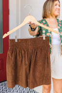 Brown corduroy shorts on a hanger with a person in the background