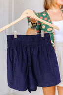 Navy blue corduroy shorts on a hanger with a blurred background