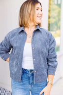 Woman wearing a gray corduroy shirt / jacket and jeans standing outdoors.