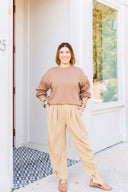 Woman in a brown sweatshirt and beige corduroy pants standing outside Laundry Dae Boutique. 