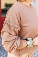 Brown sweatshirt with braided sleeves worn by a person, blurred background