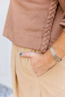 Close-up of a person wearing a brown sweatshirt with braided detail and beige pants.