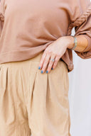 Woman in a brown sweatshirt and beige corduroy pants standing outside Laundry Dae Boutique. 