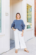 Woman wearing a gray sweatshirt with pearl embellishments and white Risen Jeans standing outside Laundry Dae Boutique.