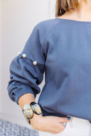 Woman wearing a gray sweatshirt with pearl embellishments, standing outside Laundry Dae Boutique.