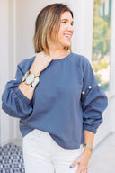 Woman wearing a gray sweatshirt with pearl embellishments, standing outside Laundry Dae Boutique.