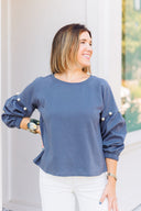 Woman wearing a gray sweatshirt with pearl embellishments, standing outside Laundry Dae Boutique.