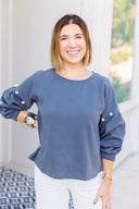 Woman wearing a gray sweatshirt with pearl embellishments, standing outside Laundry Dae Boutique.