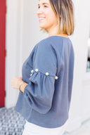 Woman wearing a gray sweatshirt with pearl embellishments, standing outside Laundry Dae Boutique.