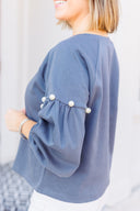 Woman wearing a gray sweatshirt with pearl embellishments, standing outside Laundry Dae Boutique.