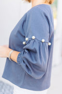 Woman wearing a gray sweatshirt with pearl embellishments, standing outside Laundry Dae Boutique.