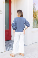 Woman wearing a gray sweatshirt with pearl embellishments and white Risen Jeans standing outside Laundry Dae Boutique.