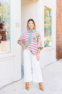 Woman wearing a colorful striped sweatshirt and white Risen Jeans standing in front of a building with large windows.