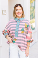 Woman wearing a colorful striped sweatshirt with floral patterns in an outdoor setting.