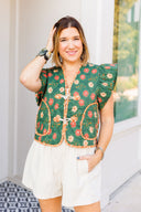 Woman wearing a green floral embroidered vest over a white outfit, standing outdoors.