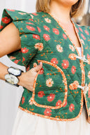Green floral-patterned vest with a close-up of a hand wearing a bracelet.
