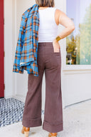 Woman in white tank top and brown jeans standing outside Laundry Dae Boutique holding blue plaid blazer.