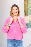 Woman wearing a pink corduroy shirt and blue jeans with a blurred outdoor background