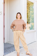 Woman in a brown sweatshirt and beige corduroy pants standing outside Laundry Dae Boutique. 