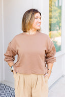 Woman wearing a brown sweatshirt and beige pants standing outdoors.