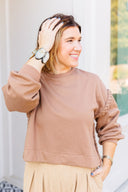 Woman wearing a brown sweatshirt and beige pants outdoors