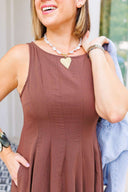 Woman wearing a brown sleeveless dress with a heart-shaped pendant necklace.