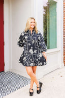 Woman wearing a black floral dress standing on a patio.