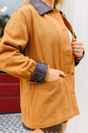 Person wearing a camel jacket with dark collar and cuffs, standing against a blurred background.