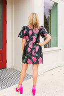 Woman wearing a floral dress with pink shoes standing in front of a house.