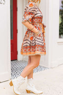 Person wearing a patterned dress and white boots standing in front of a red door.