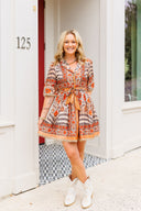Woman in a patterned dress standing outside a house with a number 125 on the door.