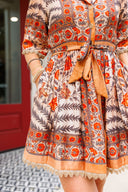 Woman wearing a patterned dress with orange and red design in an indoor setting.