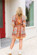 Woman wearing a patterned dress with orange accents, standing in front of a red door.