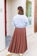 Woman wearing a light blue denim jacket and brown bubble skirt standing in front of Laundry Dae boutique.