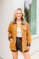 Woman wearing a brown jacket with black accents and leather shorts standing outdoors.
