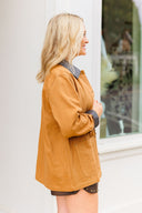 Woman wearing a camel coat standing in front of a window.
