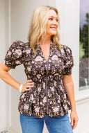 Woman wearing a floral blouse with puff sleeves standing outdoors.