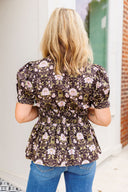 Woman wearing a floral blouse with puff sleeves in an outdoor setting.