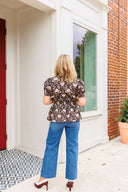 Woman in a floral blouse and blue jeans standing outside a house.