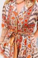 Woman wearing a floral dress with orange and red patterns on a plain background