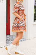 Person wearing a patterned dress and white boots standing in front of a red door.