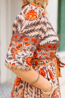 Woman wearing a patterned dress with orange and beige colors, holding a clutch.